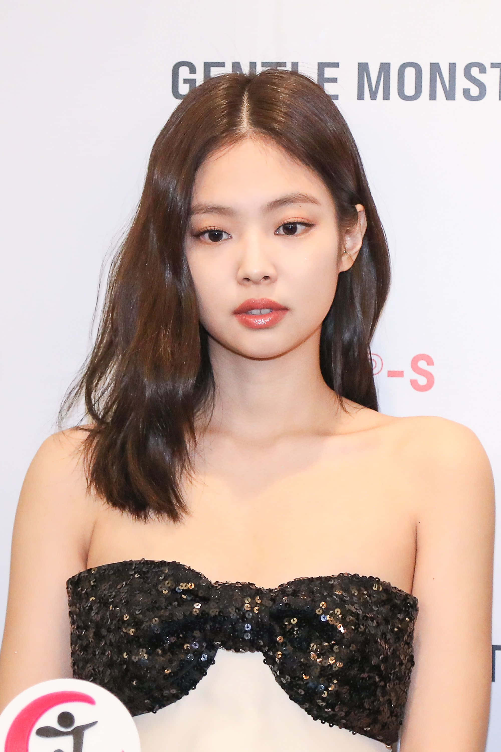 BLACKPINK 桌布 壁紙 — 一位留著及肩棕色長髮的女性，在白色品牌背景前穿著黑色亮片露肩上衣。