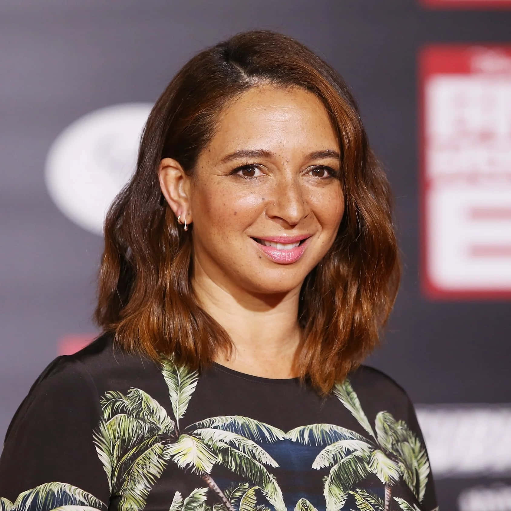 Celebrity 桌布 壁紙 — 一位留著及肩棕色頭髮的女性，身穿帶有綠色棕櫚樹圖案的黑色上衣，露出溫暖的笑容。