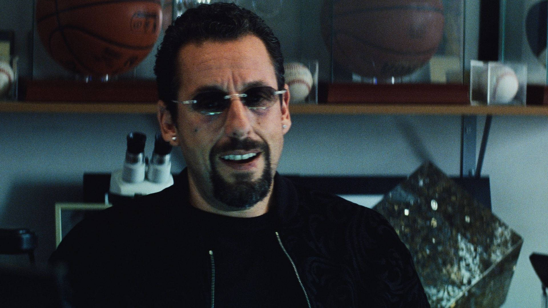 Adam Sandler 桌布 壁紙 — 一位留著山羊鬍、戴眼鏡的男士在身後架子上放有體育紀念品的房間裡微笑。