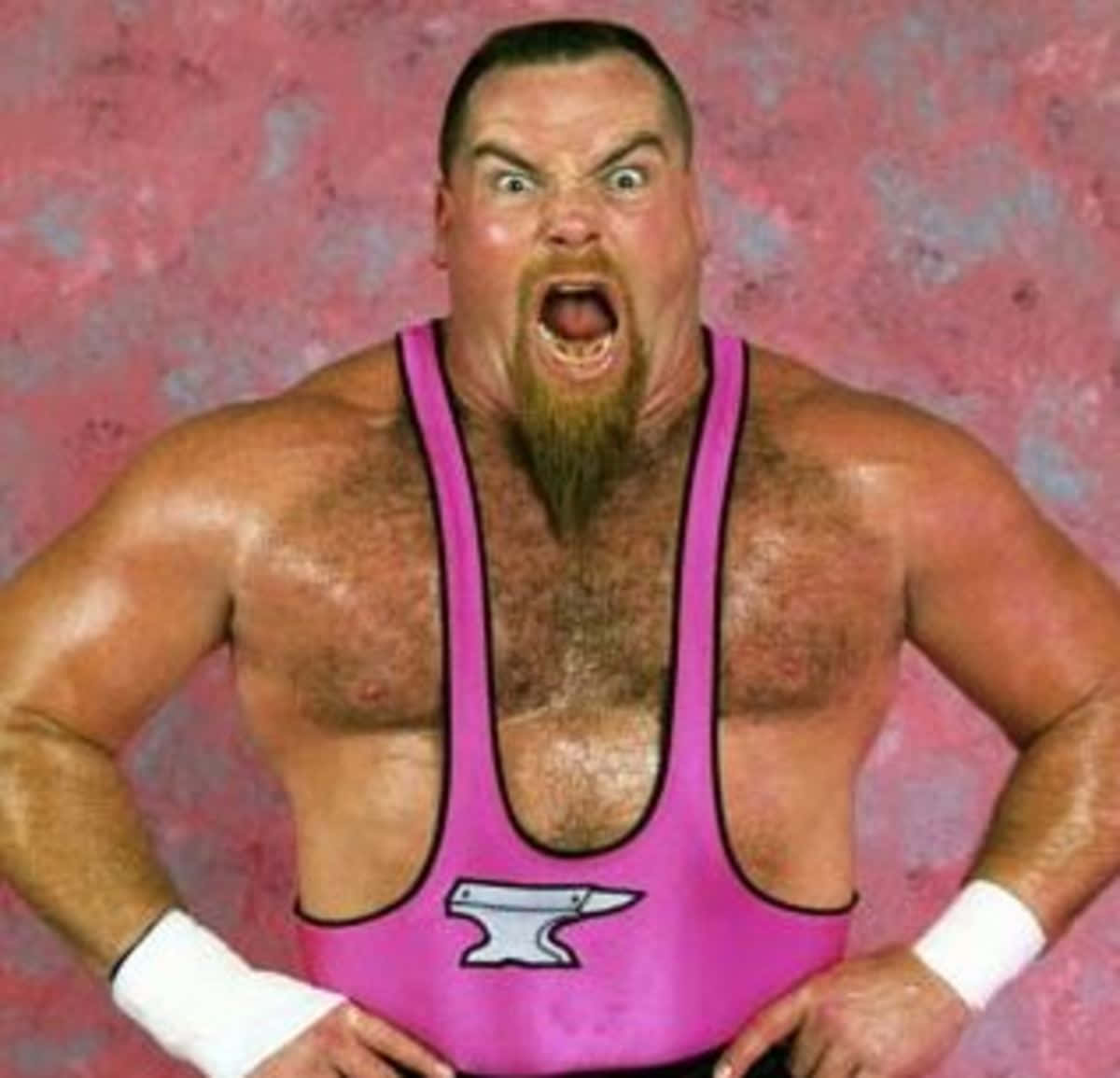 Wrestling 桌布 壁紙 — 一位留著山羊鬍的肌肉發達摔角手，穿著亮粉紅色緊身衣，在帶有紋理的粉紅色背景前猛烈尖叫。