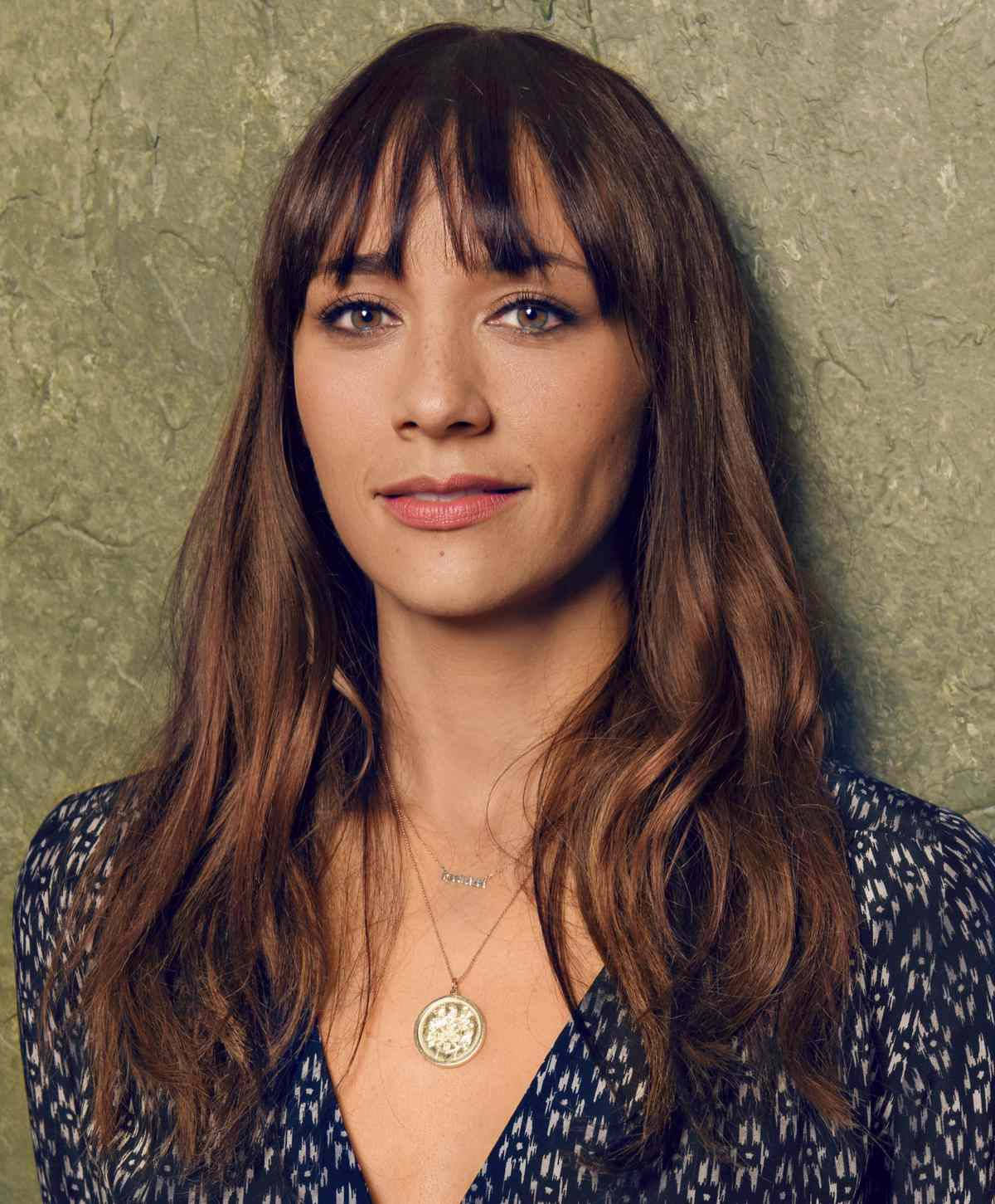 Celebrity 桌布 壁紙 — 一位留著棕色長髮和瀏海的女性，穿著圖案上衣和吊墜項鍊，背景是帶有紋理的綠色牆壁。