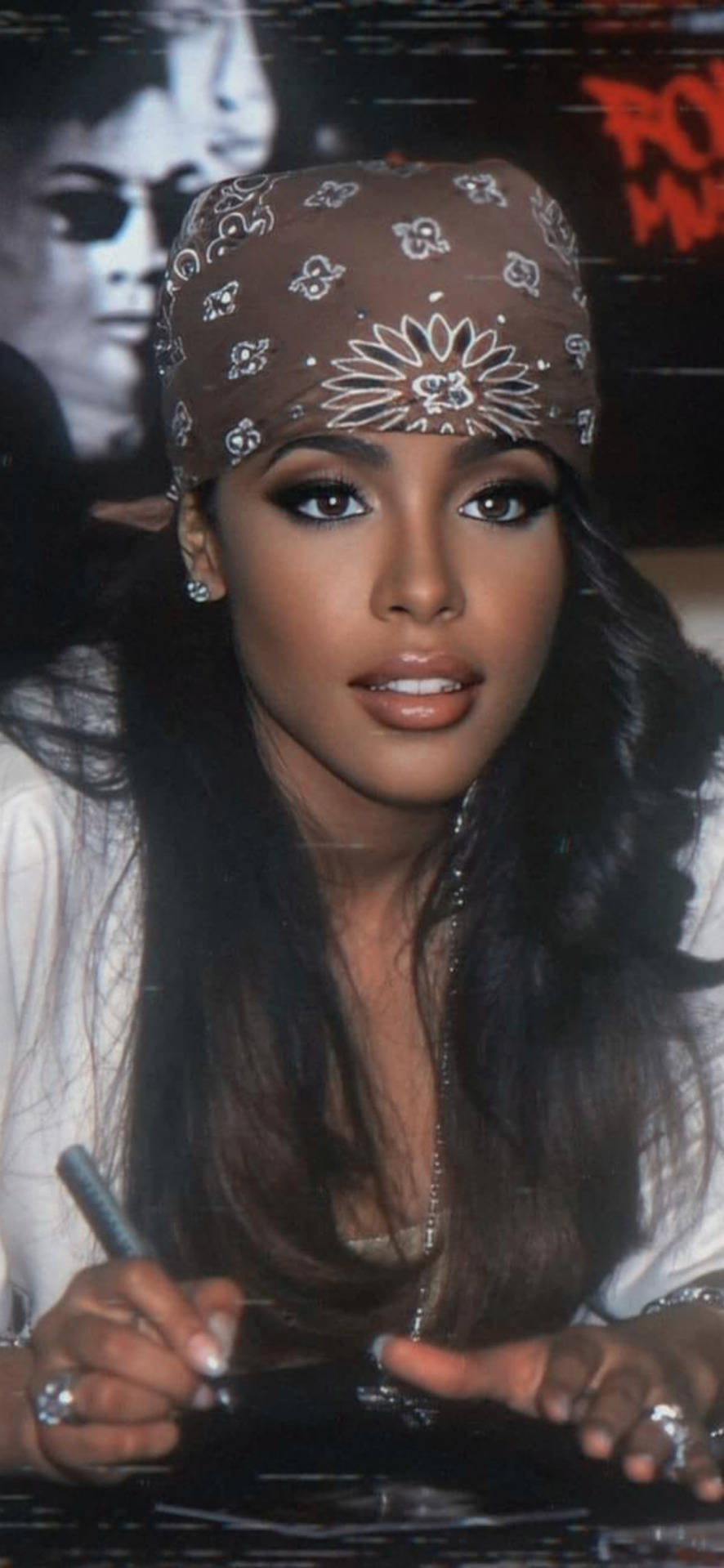 aaliyah 桌布 壁紙 — 一位留著深色長髮、戴著棕色圖案頭巾的女性，正在桌上用筆簽名。