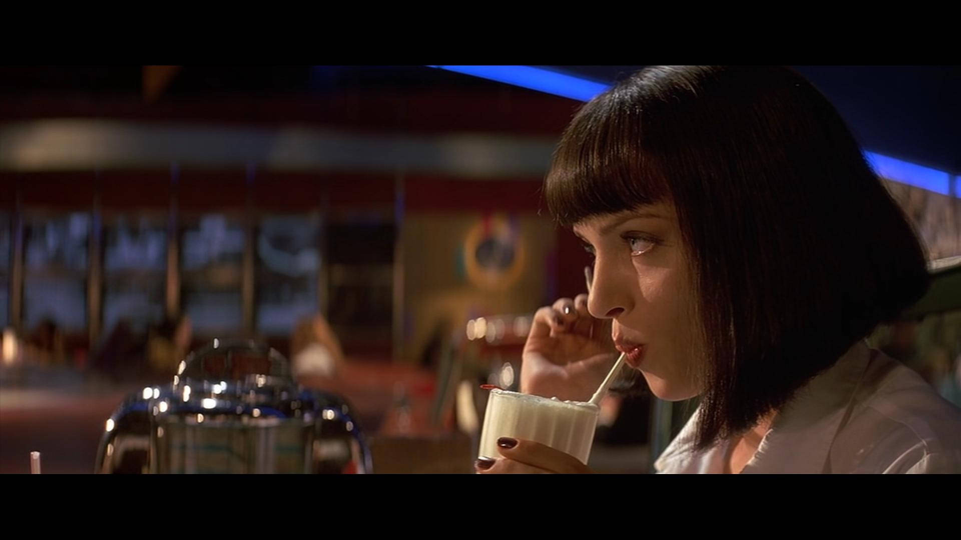 Pulp Fiction 桌布 壁紙 — 一位留著深色鮑伯頭的女士在昏暗的餐廳裡，透過吸管啜飲著奶油奶昔，周圍有溫暖的環境燈光。