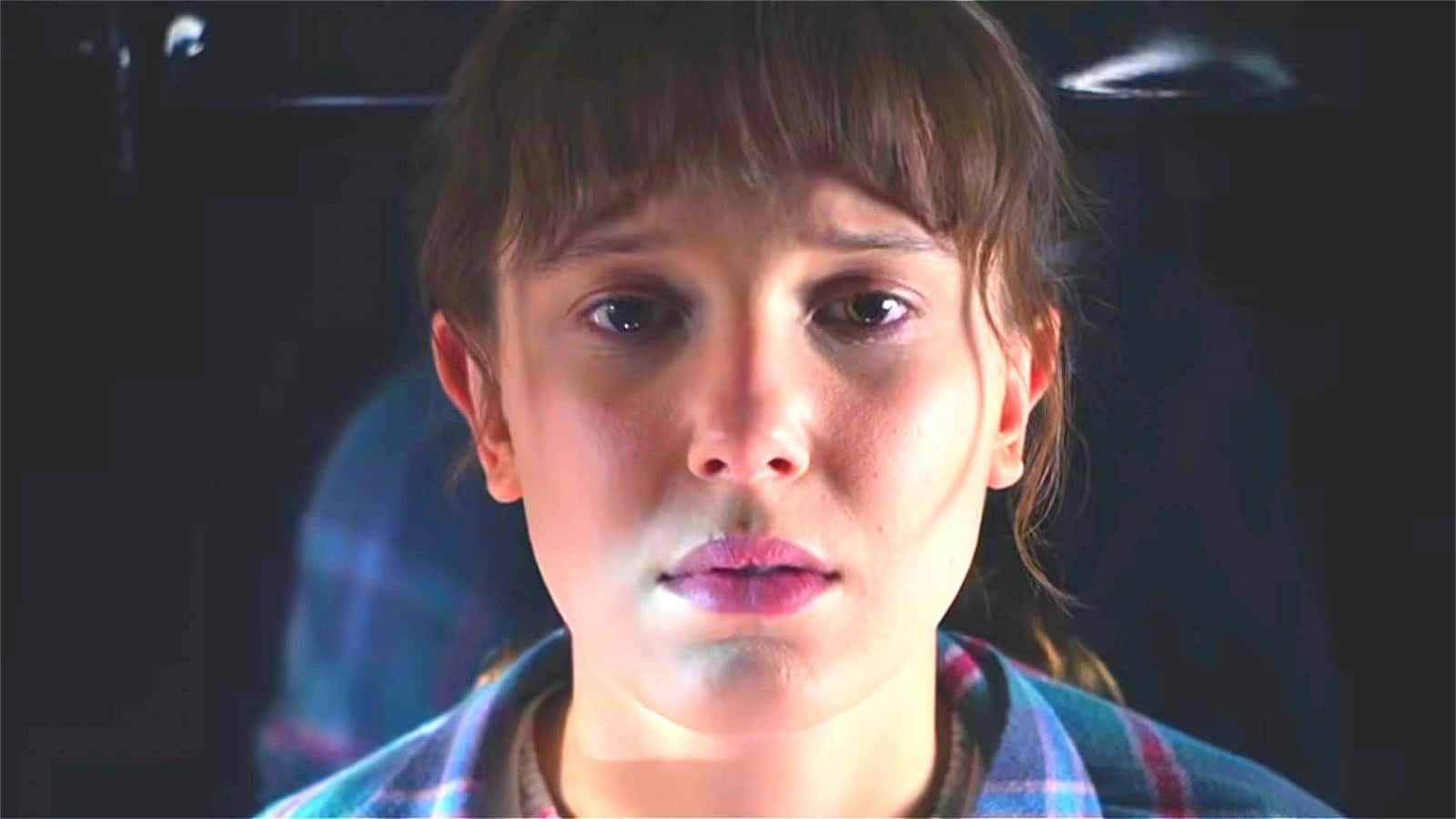 Eleven Stranger Things 桌布 壁紙 — 一位留著瀏海、身穿格紋襯衫的年輕女性，在戲劇性的燈光下專注地向前凝視。