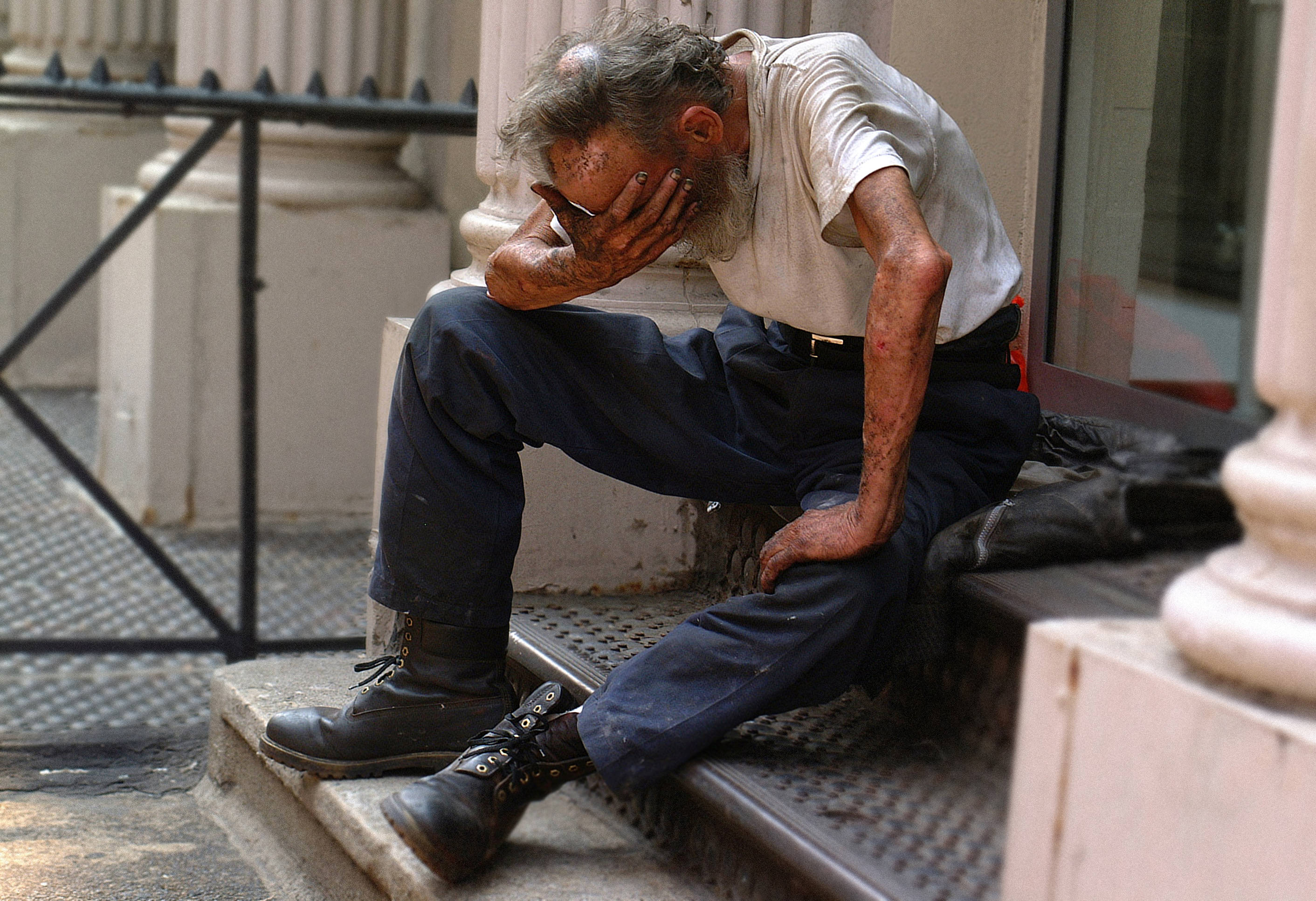 dying 桌布 壁紙 — 一位留著灰白鬍子的老人，頹然坐在城市樓梯上，雙手抱頭，身穿污漬襯衫和靴子。