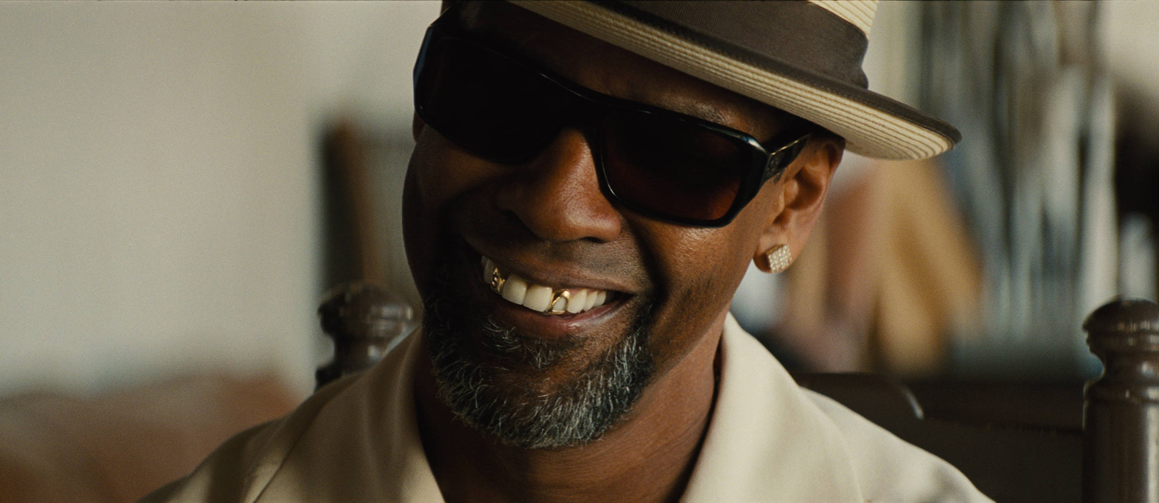 Denzel Washington 桌布 壁紙 — 一位留著灰色鬍鬚、戴著金牙套的男子，在室內戴著軟呢帽和太陽眼鏡，露出溫暖的笑容。