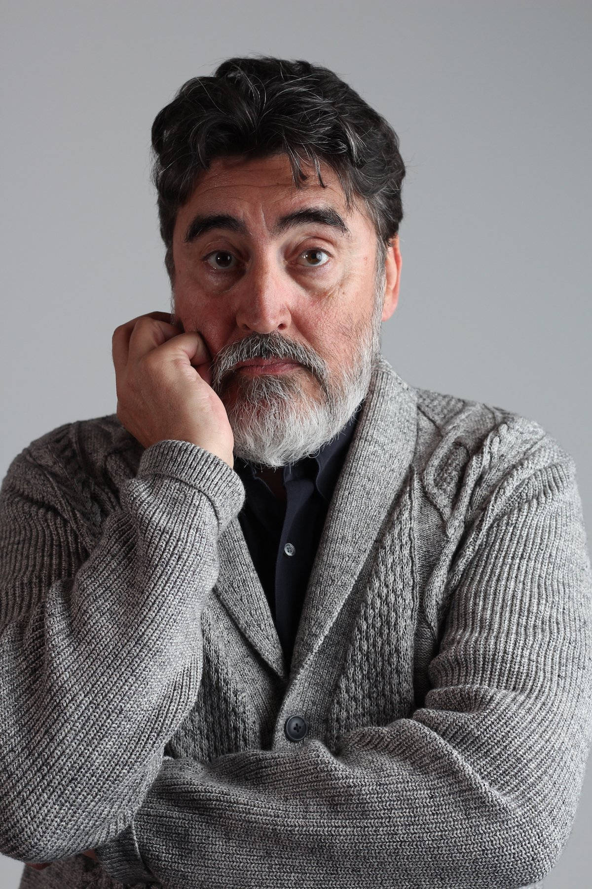 actor 桌布 壁紙 — 一位留著灰色鬍鬚的中年男子，在純灰色背景前用手托著下巴，眼神專注。