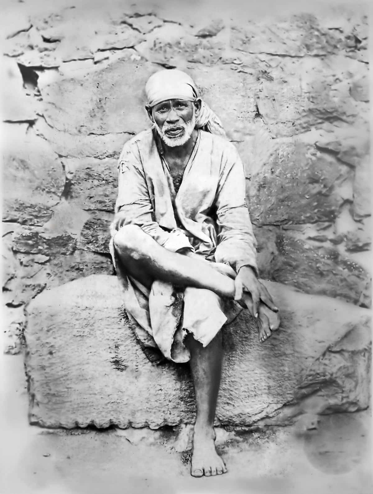 Indian 桌布 壁紙 — 一位留著白鬍子、戴頭巾的長者赤腳坐在石壁前的石台上，這是一張復古黑白照片。