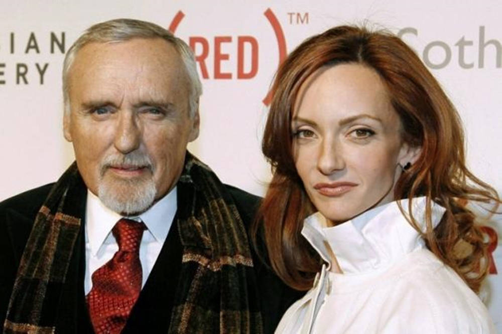 actor 桌布 壁紙 — 一位留著白鬍子的年長男士和一位紅髮女士在慈善活動中，以品牌背景板為襯托一起擺姿勢。