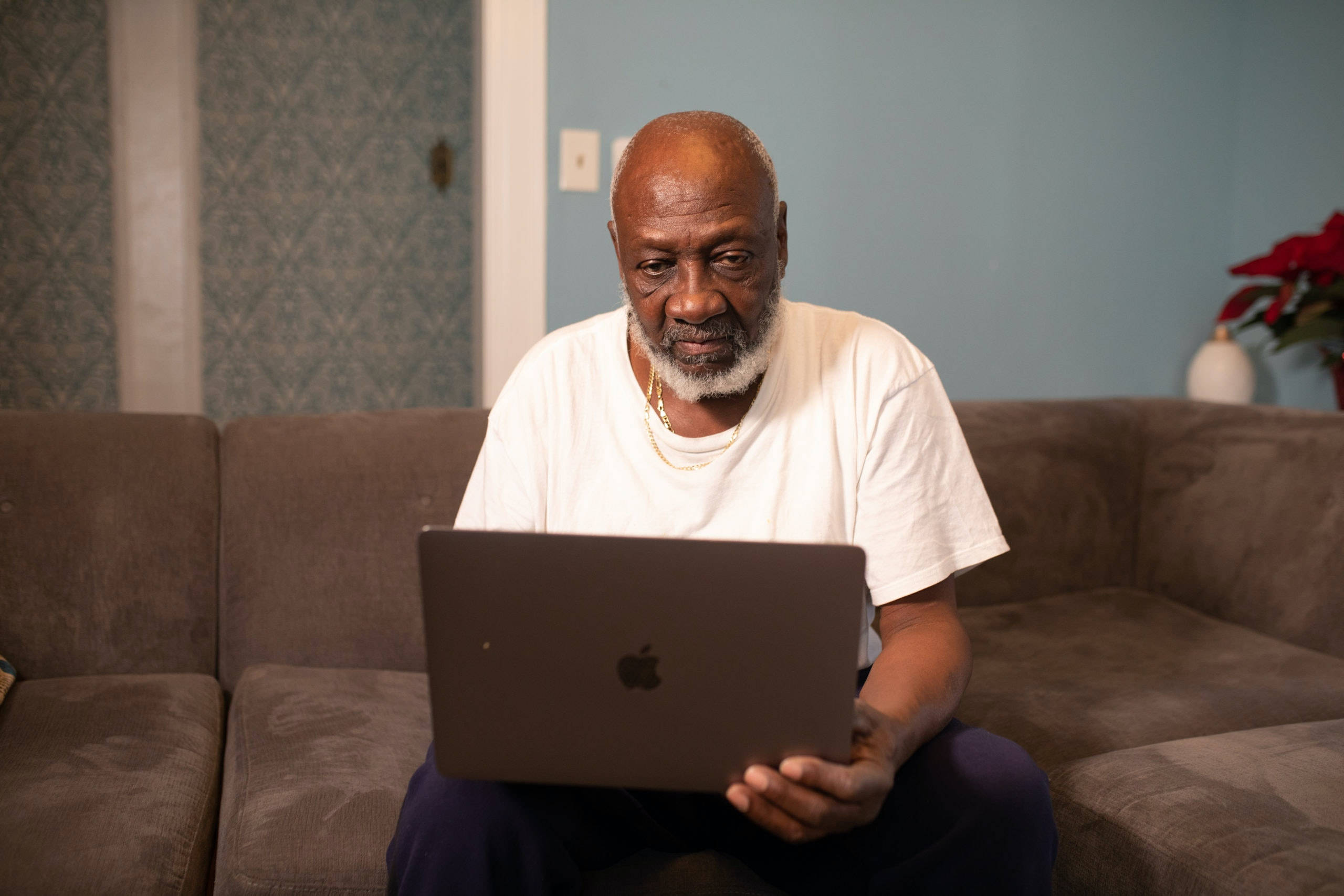 MacBook 動態圖片 桌布 壁紙 — 一位留著白鬍子的老人坐在棕色沙發上，拿著筆記型電腦，溫柔地看著鏡頭。
