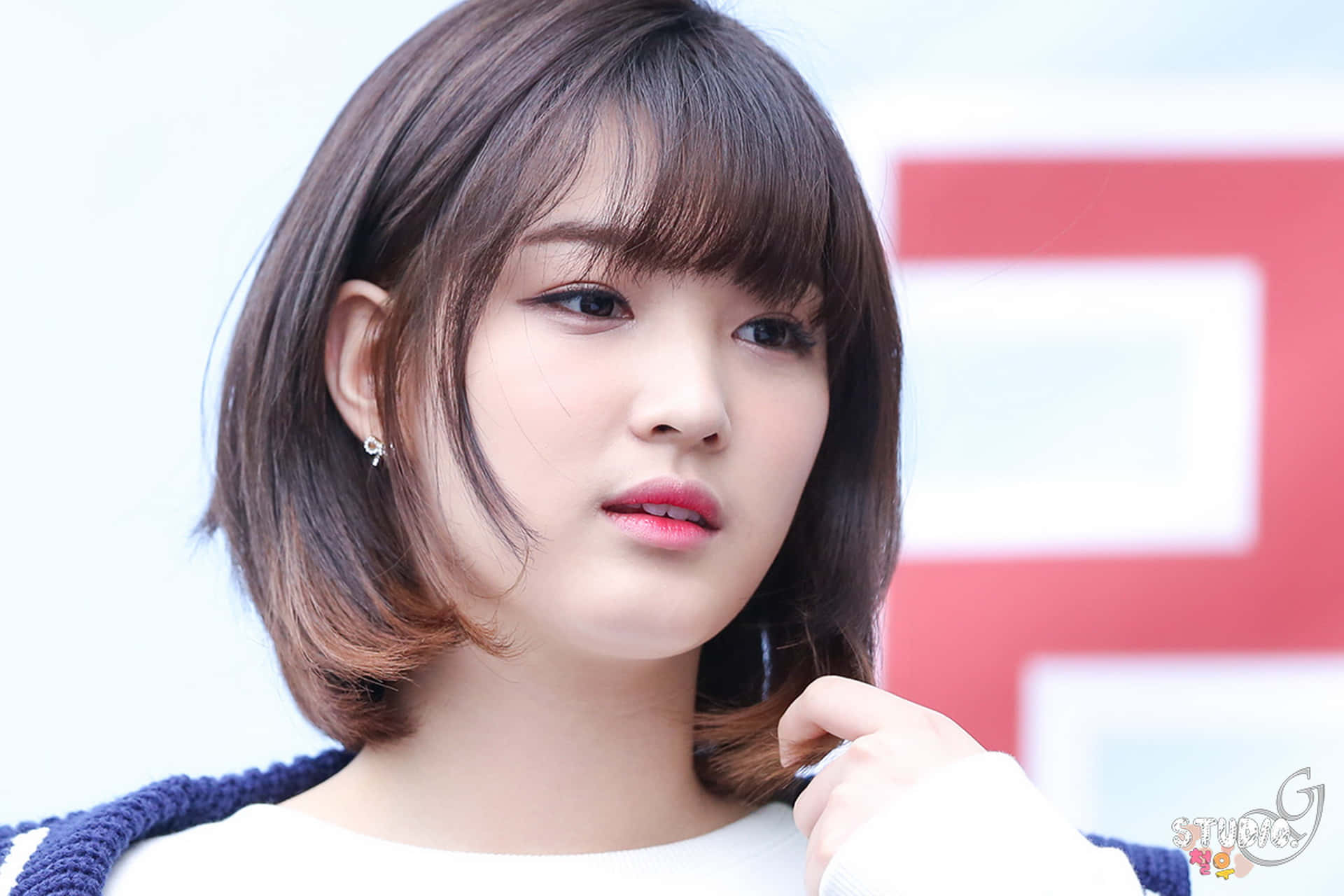 Korean Girl 桌布 壁紙 — 一位留著短棕色鮑伯頭和瀏海的年輕女性，在模糊的紅白背景下若有所思地整理頭髮。