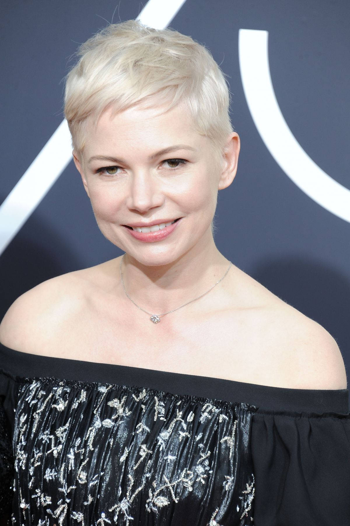 Celebrity 桌布 壁紙 — 一位留著短白金髮的女性，身穿帶有銀色刺繡的黑色露肩連衣裙，溫暖地微笑。