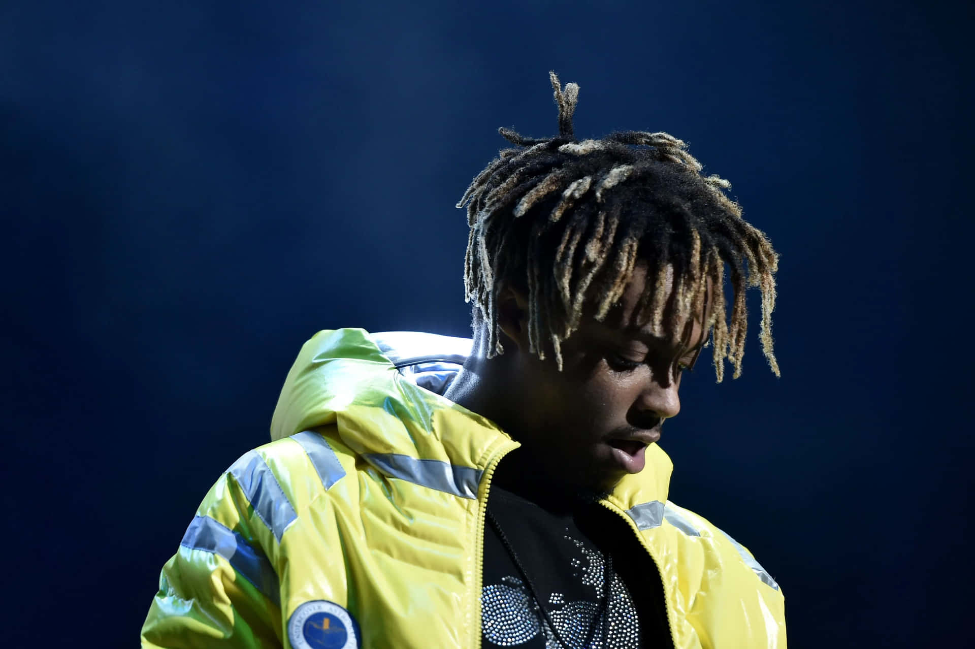 年輕表演者穿著黃色反光外套，在藍色舞台燈光下 — Juice Wrld 壁紙