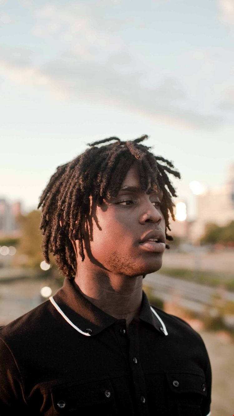 Chief Keef 桌布 壁紙 — 一位留著辮子的年輕男子在黃金時刻，對著柔和模糊的城市景觀沉思地向上凝視。