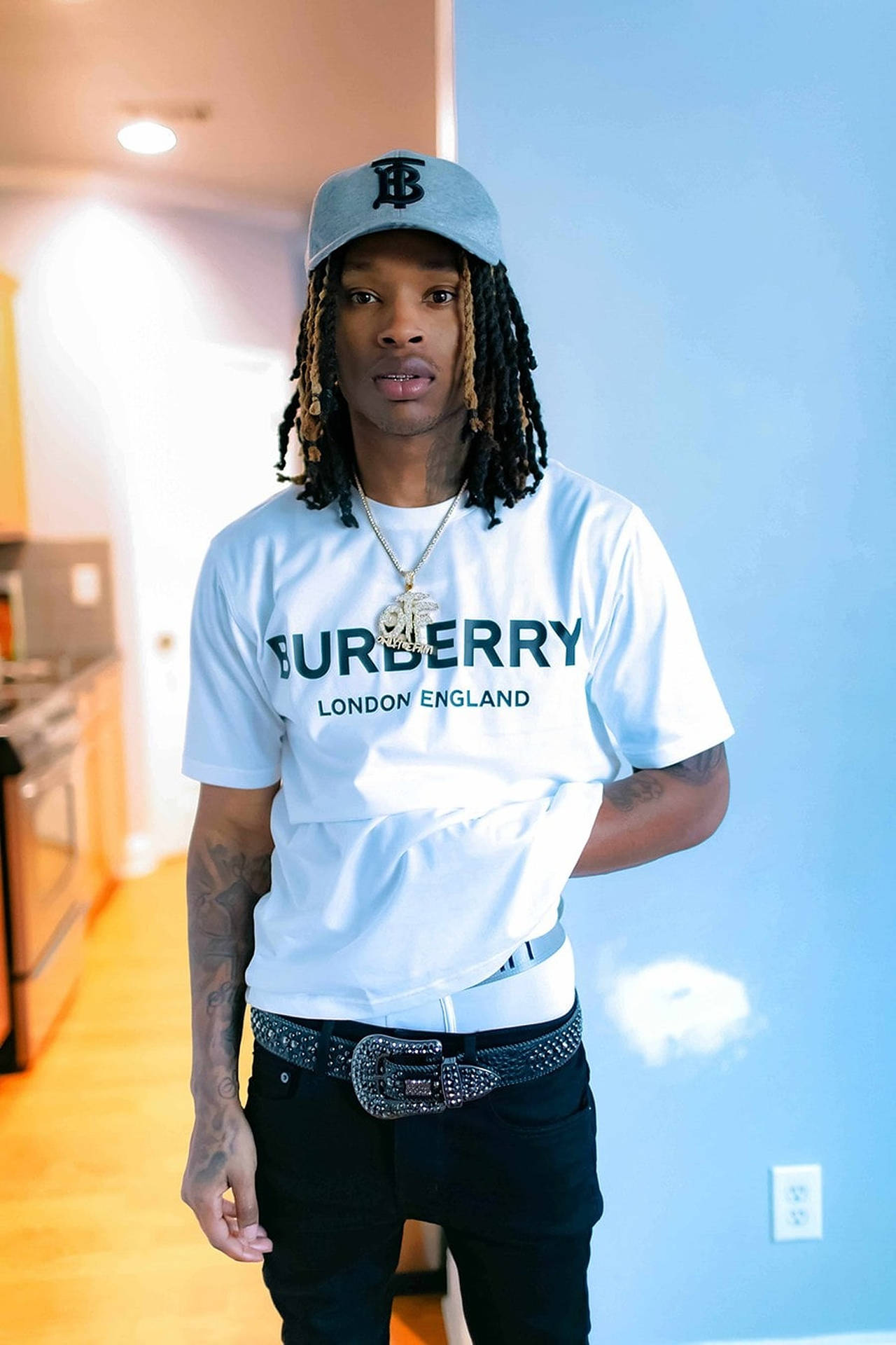 留著辮子的年輕男子在室內穿著Burberry T恤和鉚釘腰帶。 — King Von 壁紙