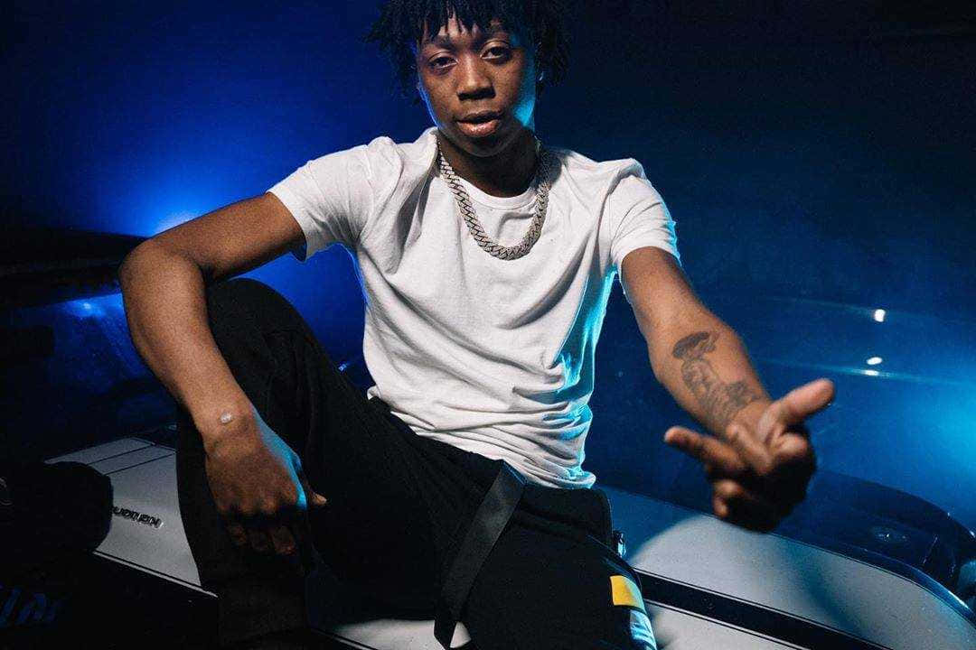 Rappers 桌布 壁紙 — 一位留著辮子的年輕男子自信地坐在汽車引擎蓋上，在強烈的藍色舞台燈光下，穿著白色T恤和金色項鍊。