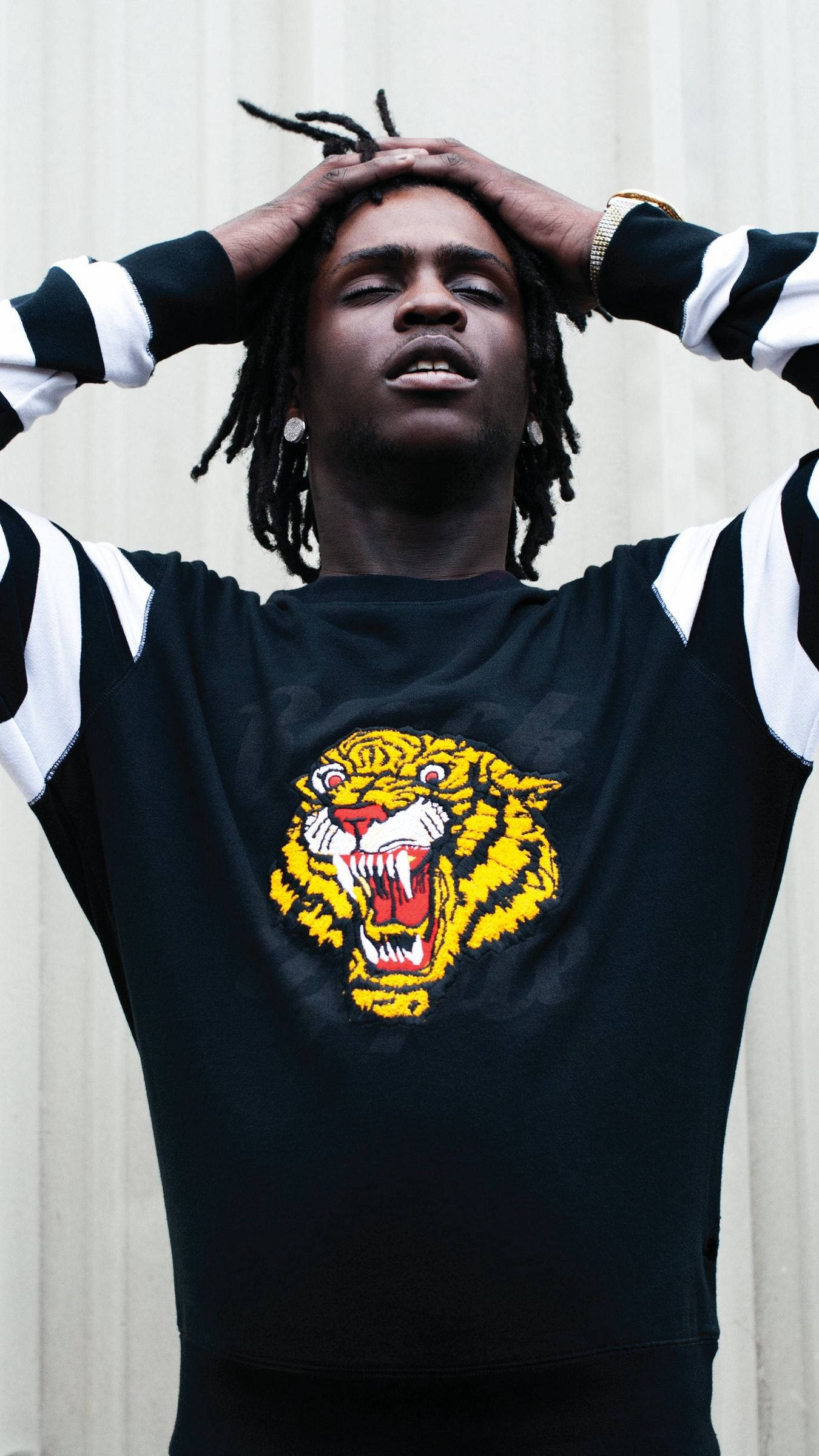 Chief Keef 桌布 壁紙 — 一位留著辮子的年輕男子雙手抱頭，身穿黑色運動衫，上面有醒目的黃色老虎圖案。