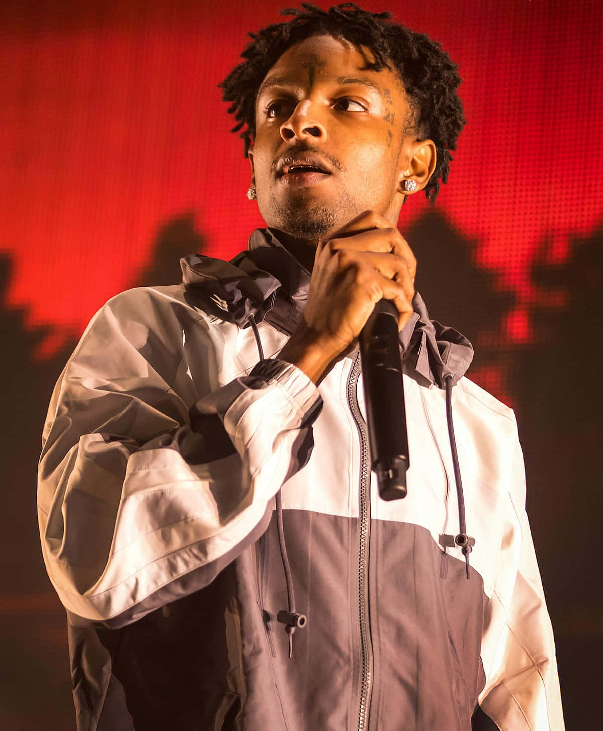 21 Savage 桌布 壁紙 — 一位留著辮子的男性表演者在強烈的紅色舞台燈光下對著麥克風唱歌。