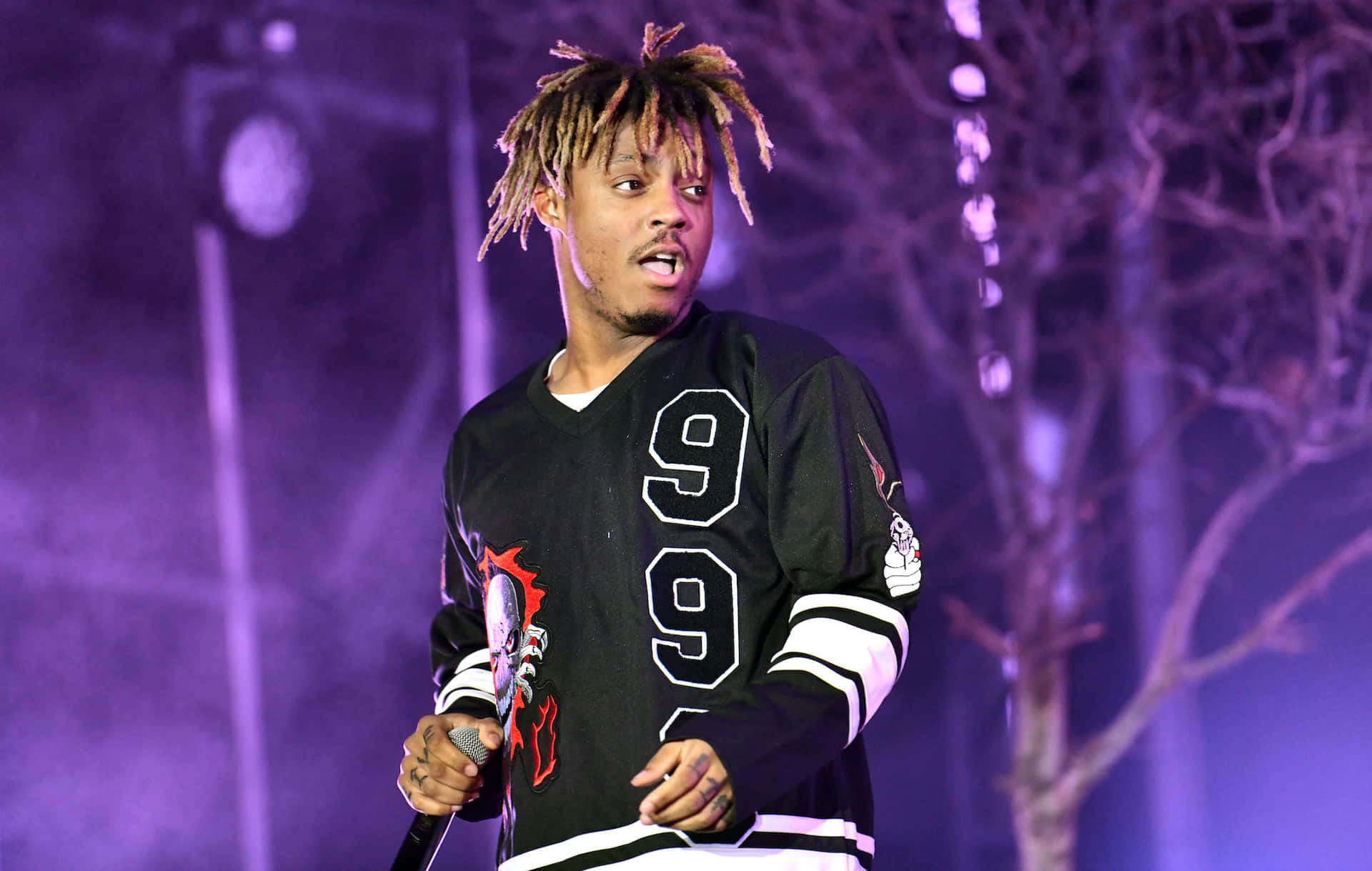 留著辮子的男歌手在夜晚的紫色燈光舞台上表演。 — Juice Wrld 壁紙