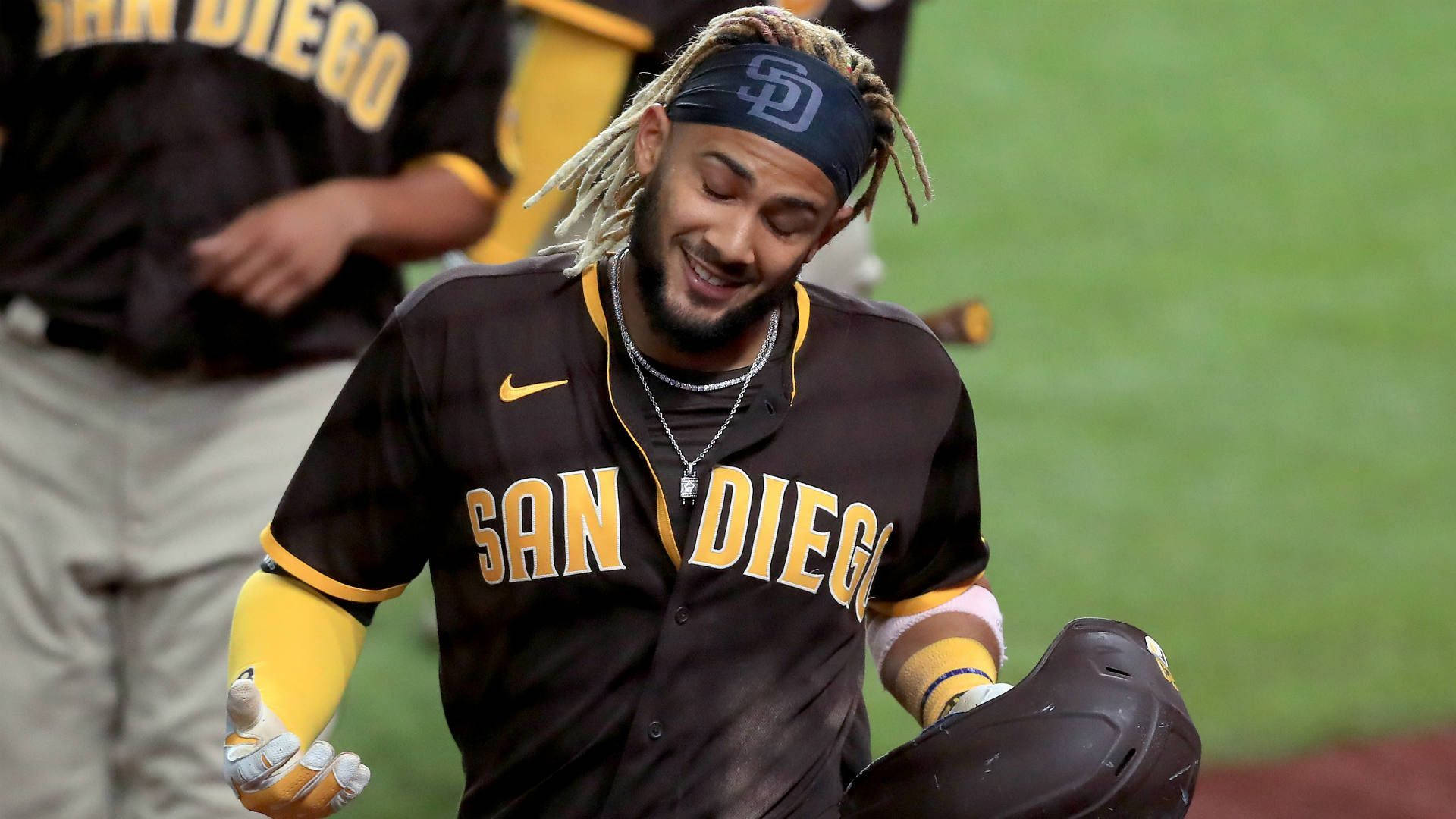 Tatis 桌布 壁紙 — 一位留著辮子的聖地牙哥教士隊棒球選手在綠色球場上微笑著拿著頭盔。