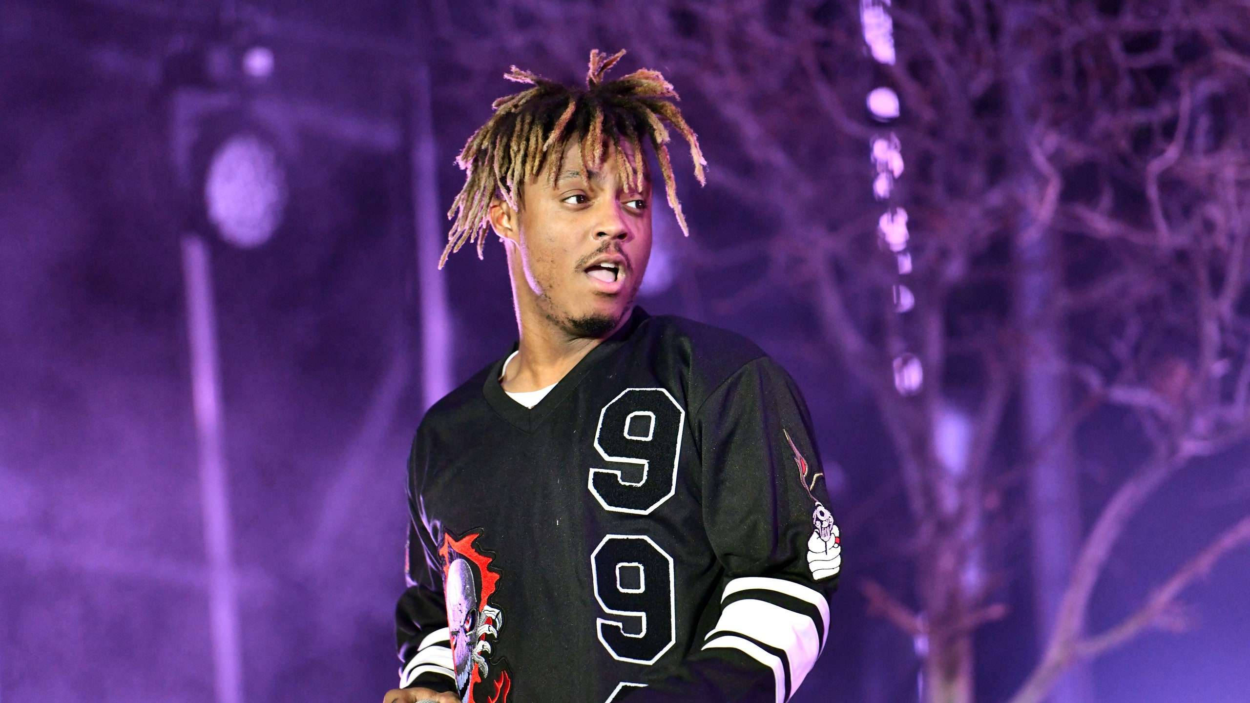 Juice Wrld Desktop 桌布 壁紙 — 一位留著辮子的表演者，身穿黑色99號球衣，夜晚站在紫色燈光照耀的舞台上。