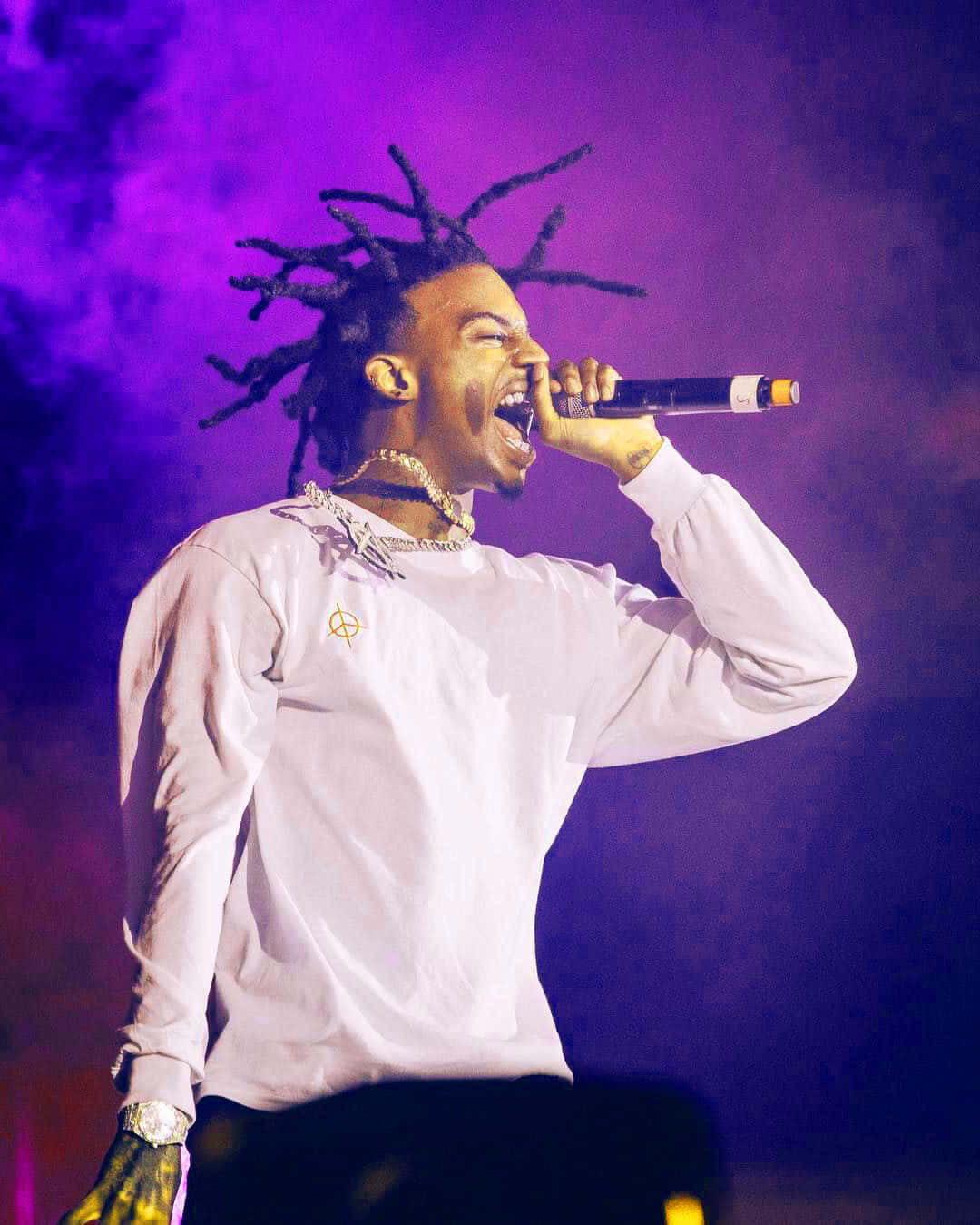Playboi Carti HD 桌布 壁紙 — 一位留著辮子的說唱歌手在充滿活力的紫色舞台燈光下，熱情地對著麥克風唱歌。