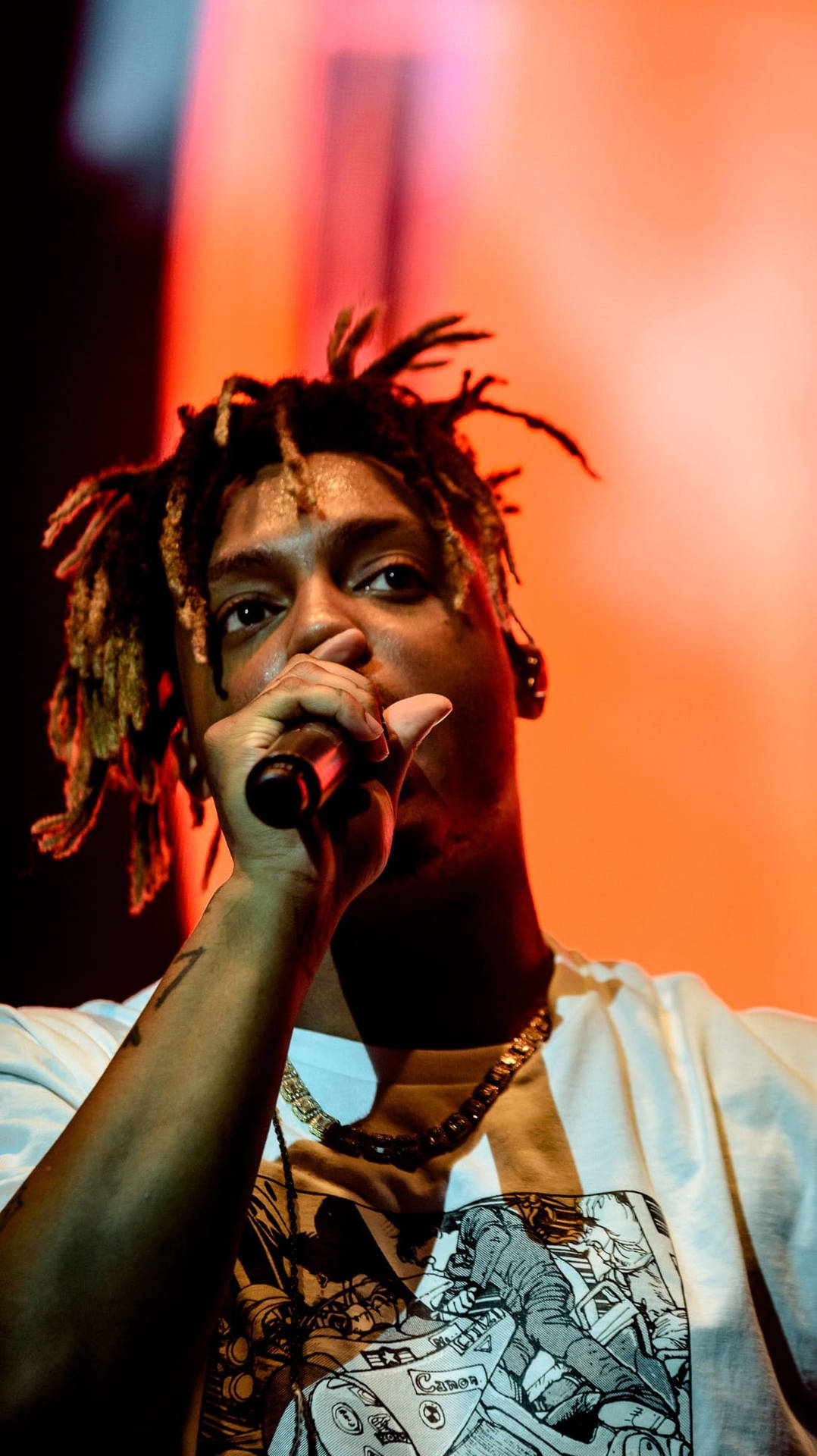 說唱歌手在舞台上表演，留著辮子，在橙色燈光下拿著麥克風。 — Juice Wrld 壁紙