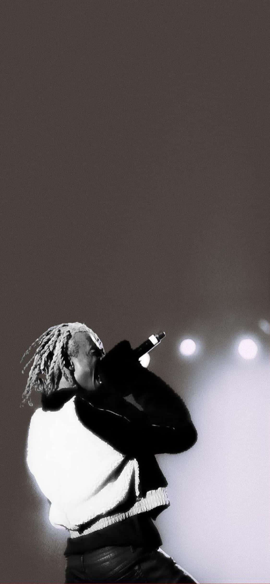 Playboi Carti iPhone 桌布 壁紙 — 一位留著辮子的音樂家在明亮的舞台燈光下對著麥克風唱歌，這是一張黑白表演照。