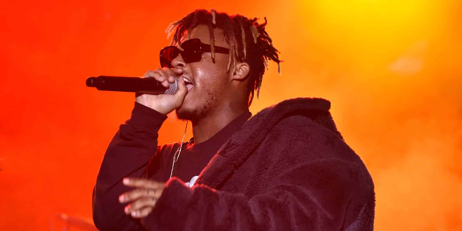 饒舌歌手在橙色燈光下，戴著太陽眼鏡和連帽衫在舞台上表演。 — Juice Wrld 壁紙