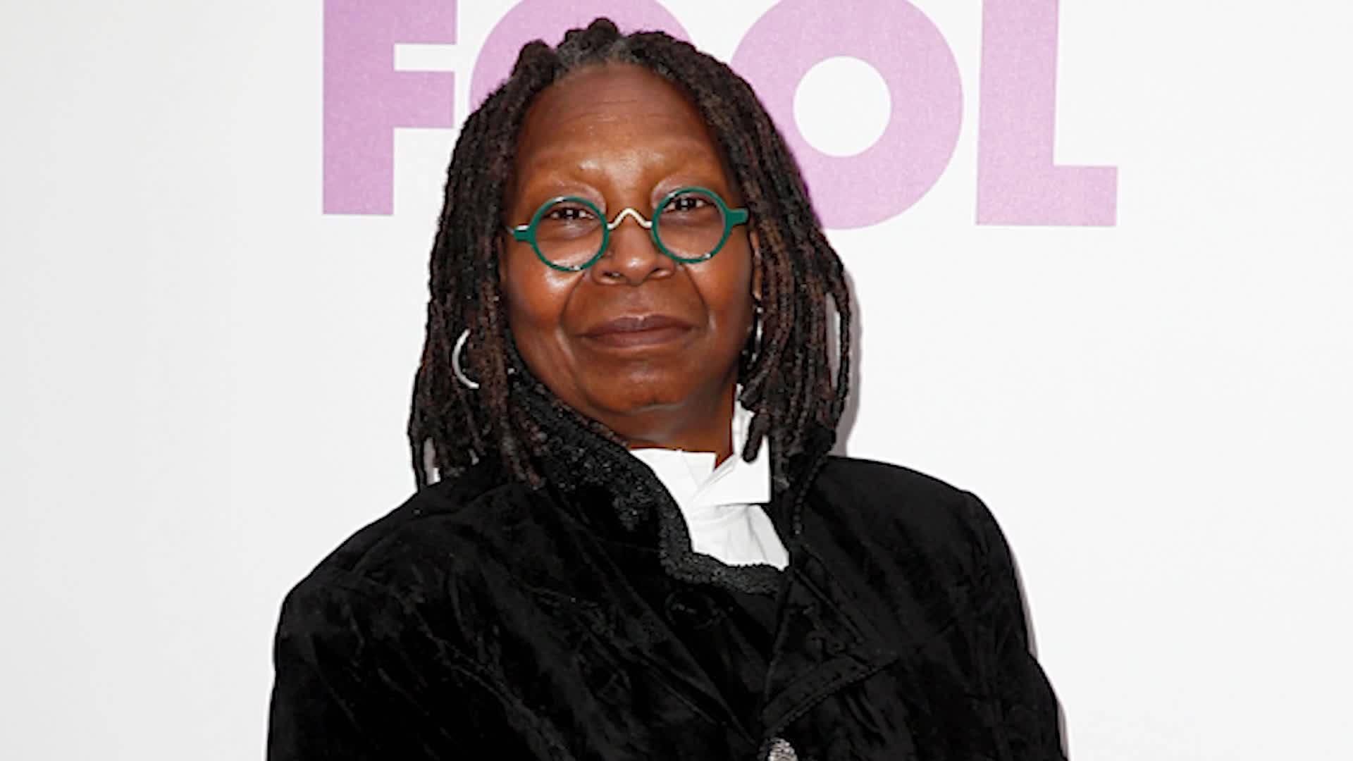 Celebrity 桌布 壁紙 — 一位留著辮子頭、戴著綠色框眼鏡的女性在粉紅色「FOOL」背景前溫暖地微笑。