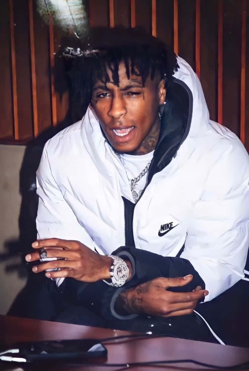 Youngboy 桌布 壁紙 — 一位留著辮子頭和刺青的年輕男子穿著白色Nike羽絨外套，在室內拿著香菸。