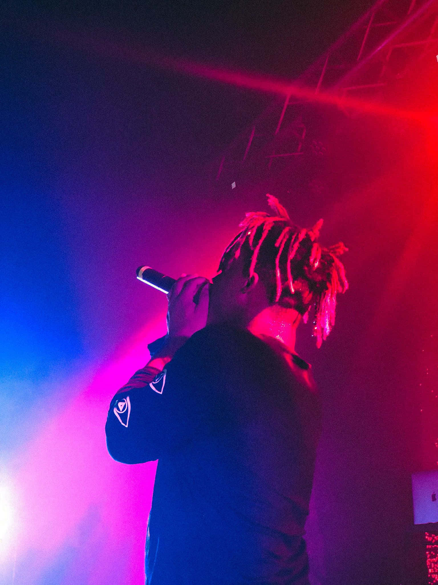 Rappers 桌布 壁紙 — 一位留著辮子頭的表演者在充滿活力的紅色和藍色舞台燈光下對著麥克風唱歌。