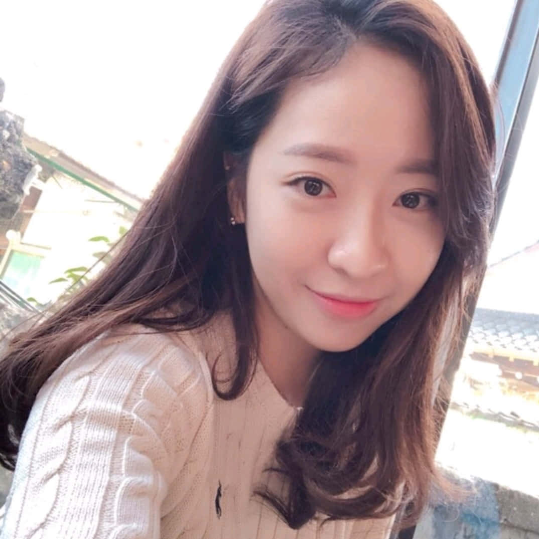 Cute Girl 桌布 壁紙 — 一位留著長長棕色頭髮的年輕女性，穿著奶油色麻花針織毛衣，溫柔地微笑。