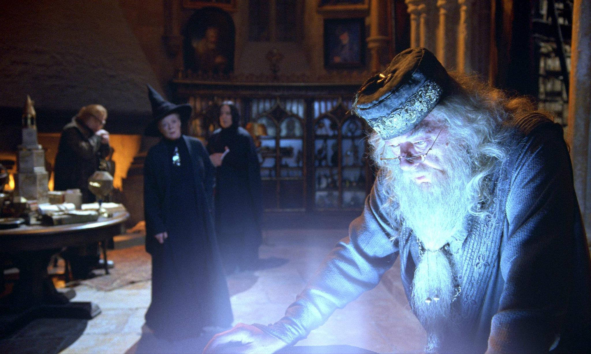 dumbledore 桌布 壁紙 — 一位留著長長白鬍鬚、戴著眼鏡的古代巫師，在一個光線昏暗、裝飾華麗的書房裡，俯身於一個發光的魔法物體之上。
