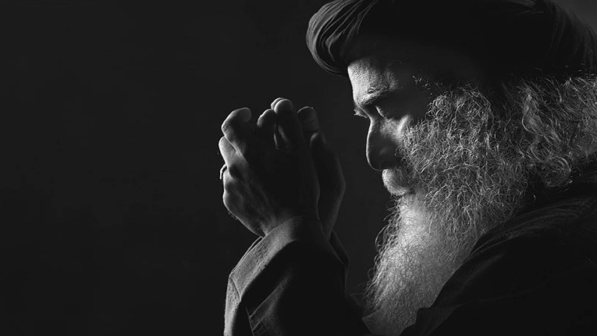 Praying 桌布 壁紙 — 一位留著長鬍鬚、戴著頭巾的莊嚴男子，在陰影單色中雙手合十，靜默祈禱。