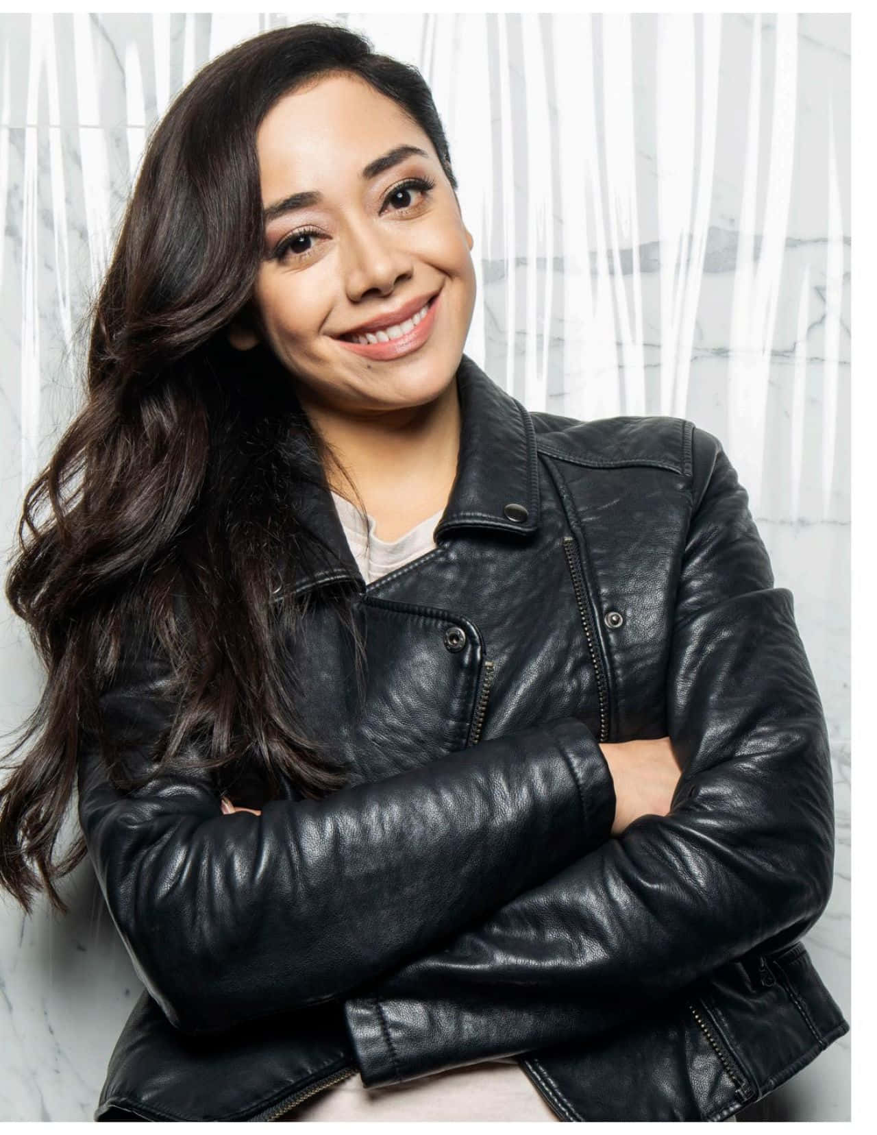 Aimee Garcia 桌布 壁紙 — 一位留著長黑髮的微笑女士，在白色大理石背景前穿著黑色皮夾克。