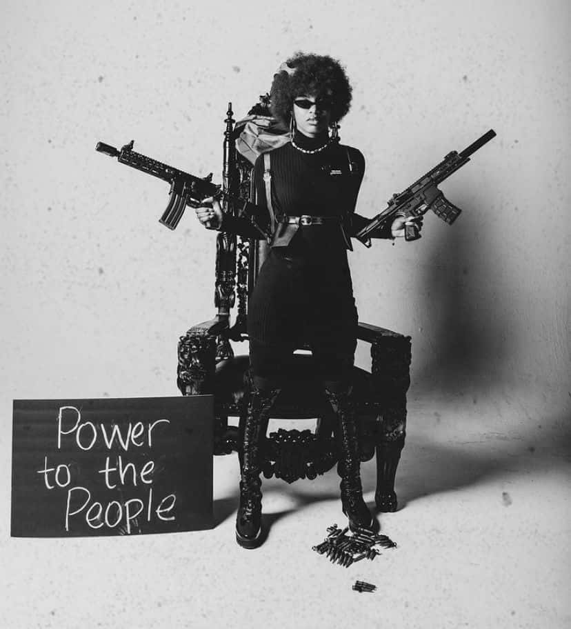 Black Panther Party 桌布 壁紙 — 一位留著非洲爆炸頭、戴著太陽眼鏡的人威嚴地坐在王座上，手持兩支步槍，旁邊有一個寫著「Power to the People」的標語牌。