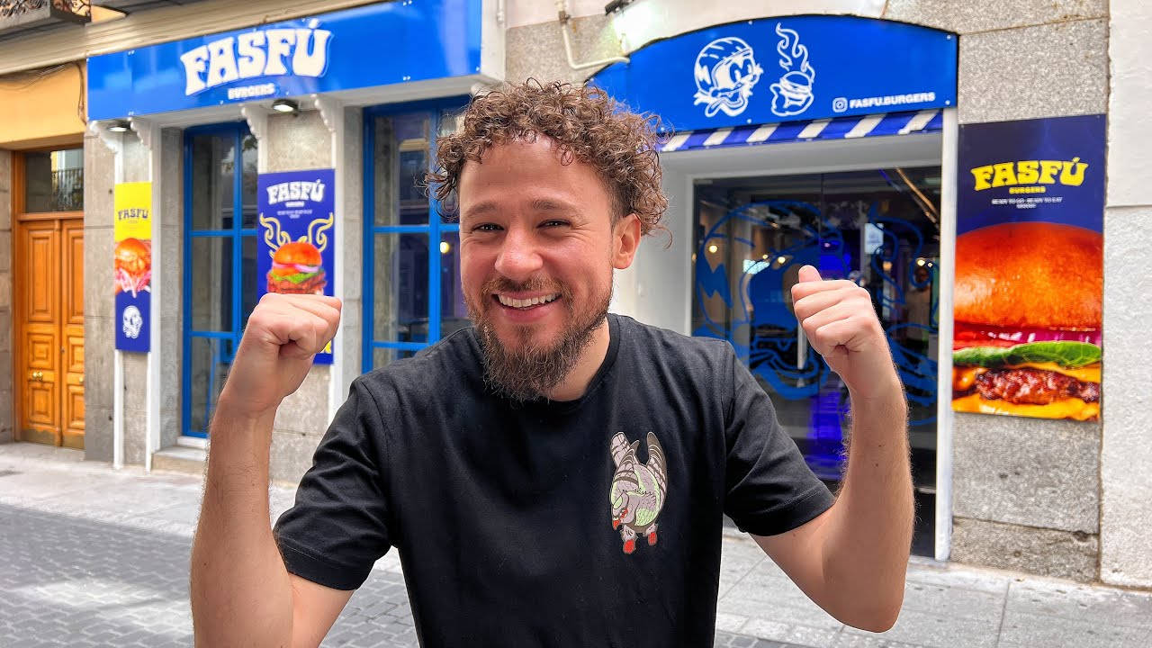 Madrid 桌布 壁紙 — 一位留著鬍鬚、捲髮的男子在明亮的藍色FASFU漢堡餐廳店面微笑並握緊拳頭。