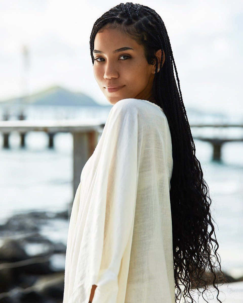 jhene aiko 桌布 壁紙 — 一位留著黑色長辮子的女性，身穿白色飄逸上衣，在俯瞰水面的碼頭旁轉身凝視鏡頭。