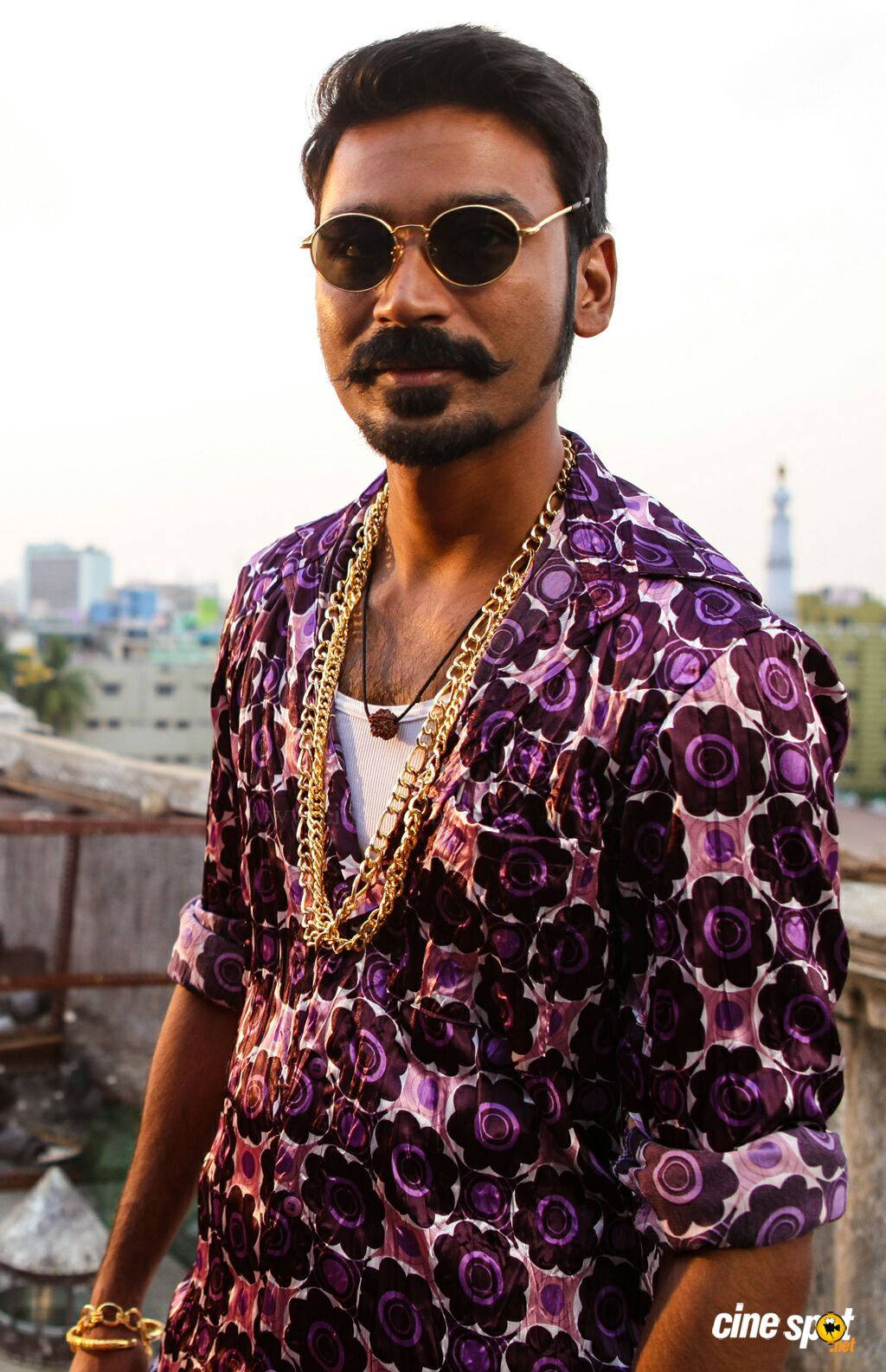 Indian 桌布 壁紙 — 一位留鬍子、戴太陽眼鏡的時尚男士，穿著紫色花卉襯衫和金色鏈條，站在可俯瞰城市景觀的屋頂上。