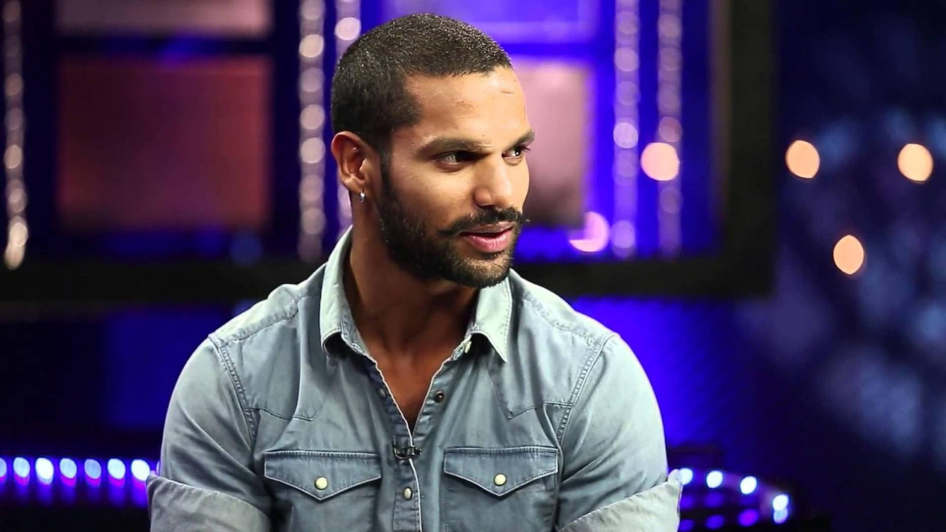 shikhar dhawan 桌布 壁紙 — 一位留鬍子、戴耳環的男子穿著牛仔襯衫，背景是模糊的紫色和藍色工作室背景，帶有散景燈光。