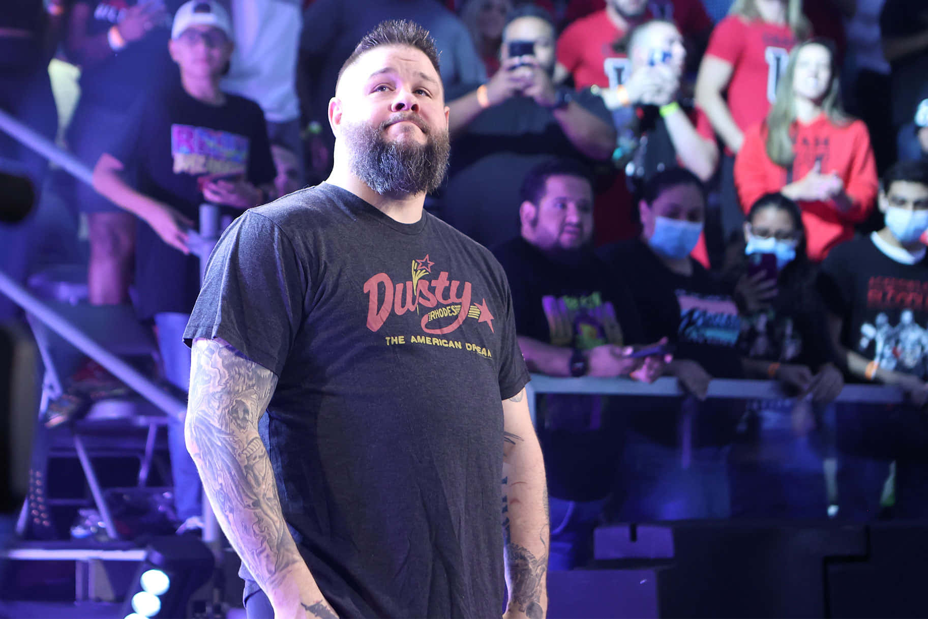 WWE 桌布 壁紙 — 一位留鬍子、有刺青的男人自信地站在燈光昏暗的競技場中，粉絲們在看台上觀看。