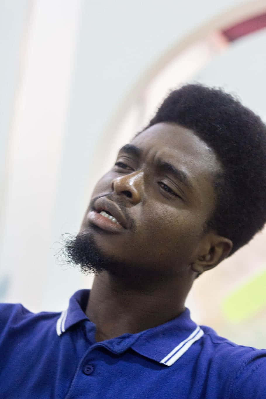 Nigeria 桌布 壁紙 — 一位留鬍子、梳非洲爆炸頭的年輕男士，身穿藍色Polo衫，向上望，背景柔和模糊。