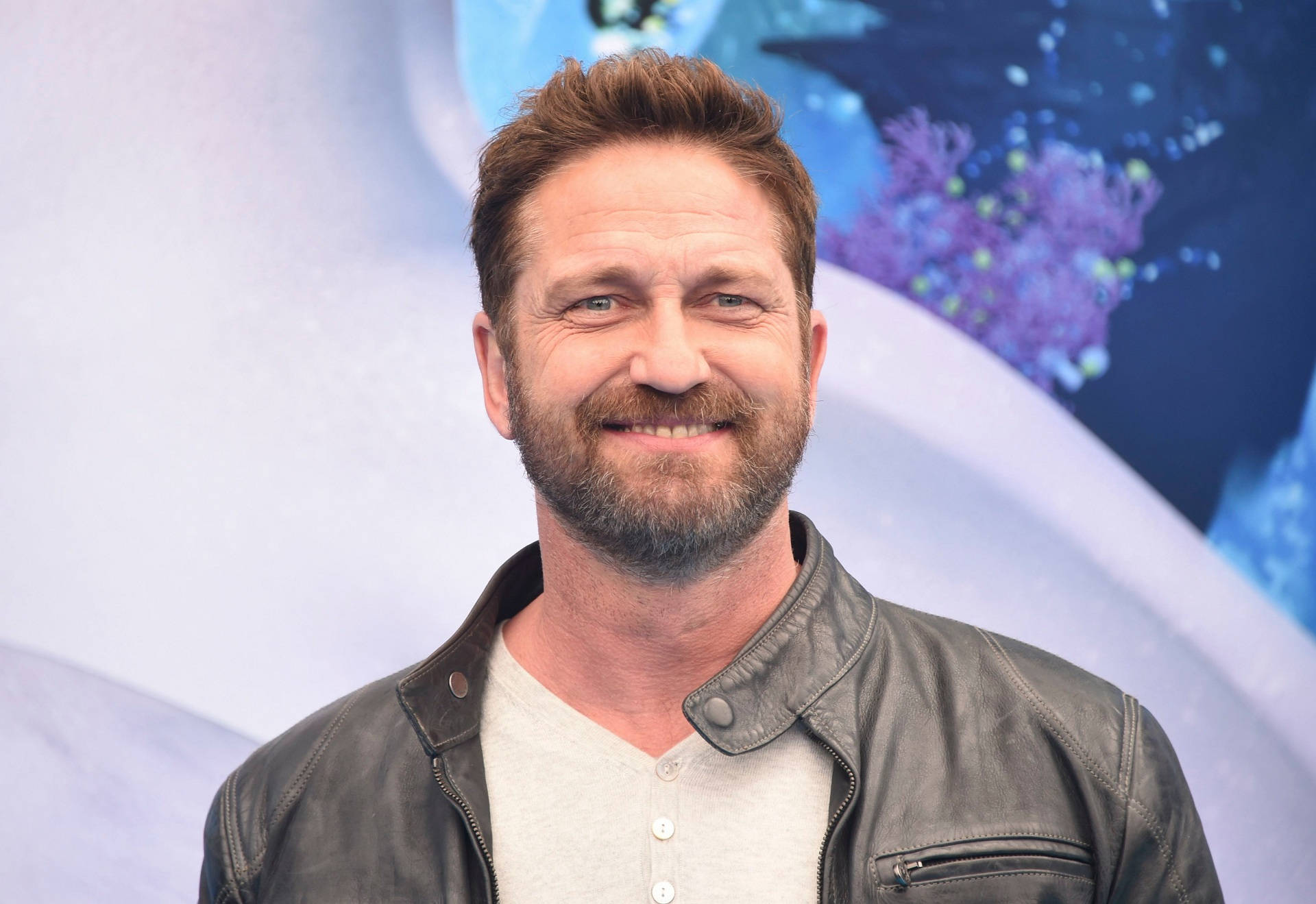 Celebrity 桌布 壁紙 — 一位留鬍子、棕色頭髮的微笑男士，穿著皮夾克，背景是色彩繽紛的抽象圖案。