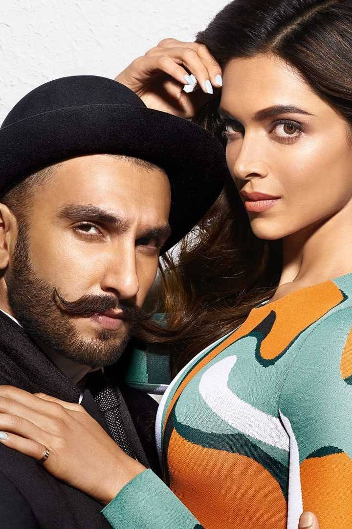 Ranveer Singh 桌布 壁紙 — 一位留鬍子戴圓頂禮帽的時尚男士，在純白牆前擁抱一位穿著彩色圖案毛衣的女士。