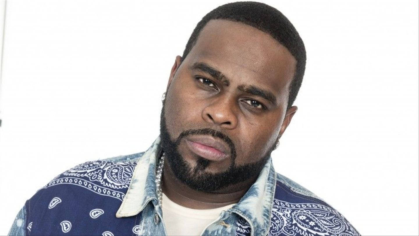 90s Rapper 桌布 壁紙 — 一位留鬍子戴耳環的男子，在純白色背景前穿著藍色佩斯利花紋襯衫。