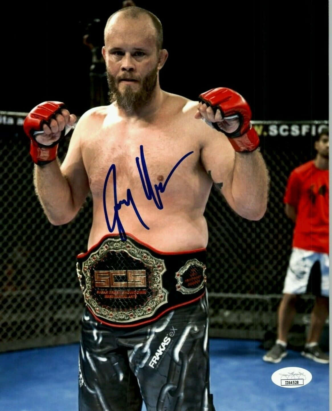 Fight 桌布 壁紙 — 一位留鬍子的MMA拳手，戴著紅色手套和冠軍腰帶，胸前有簽名，在籠中勝利地站立。