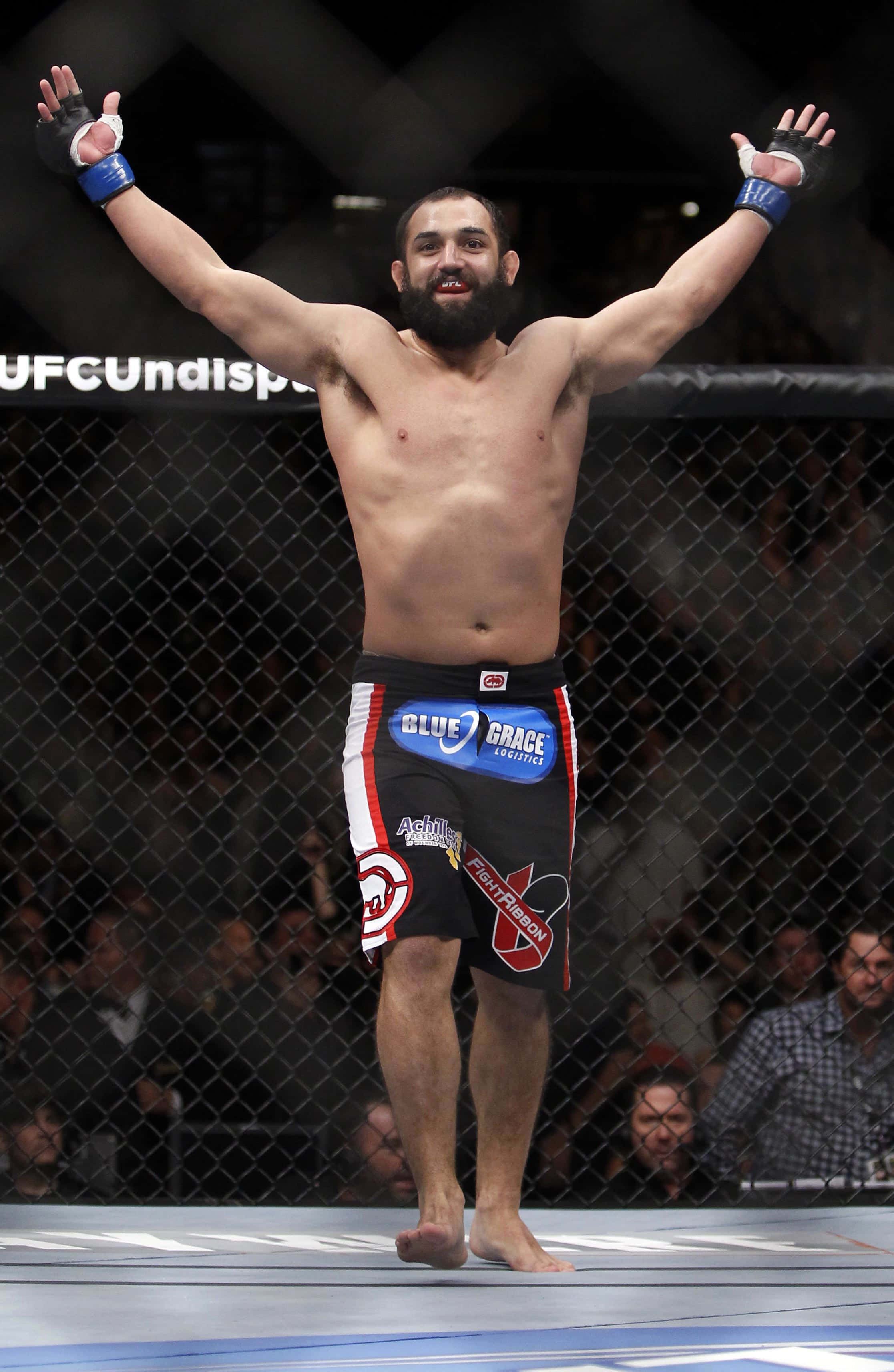 Champion 桌布 壁紙 — 一位留鬍子的MMA拳手在UFC八角籠內勝利地高舉雙臂，籠後有歡呼的人群。