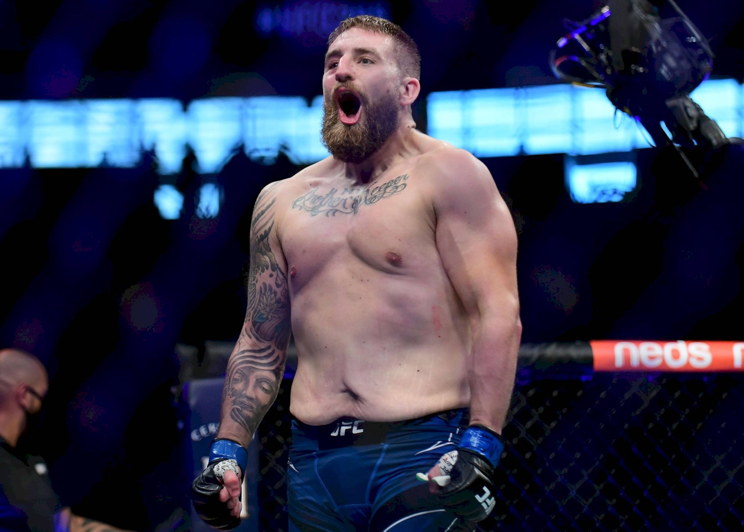 UFC 桌布 壁紙 — 一位留鬍子的MMA拳手在明亮的擂台燈光下，在八角籠中勝利咆哮。