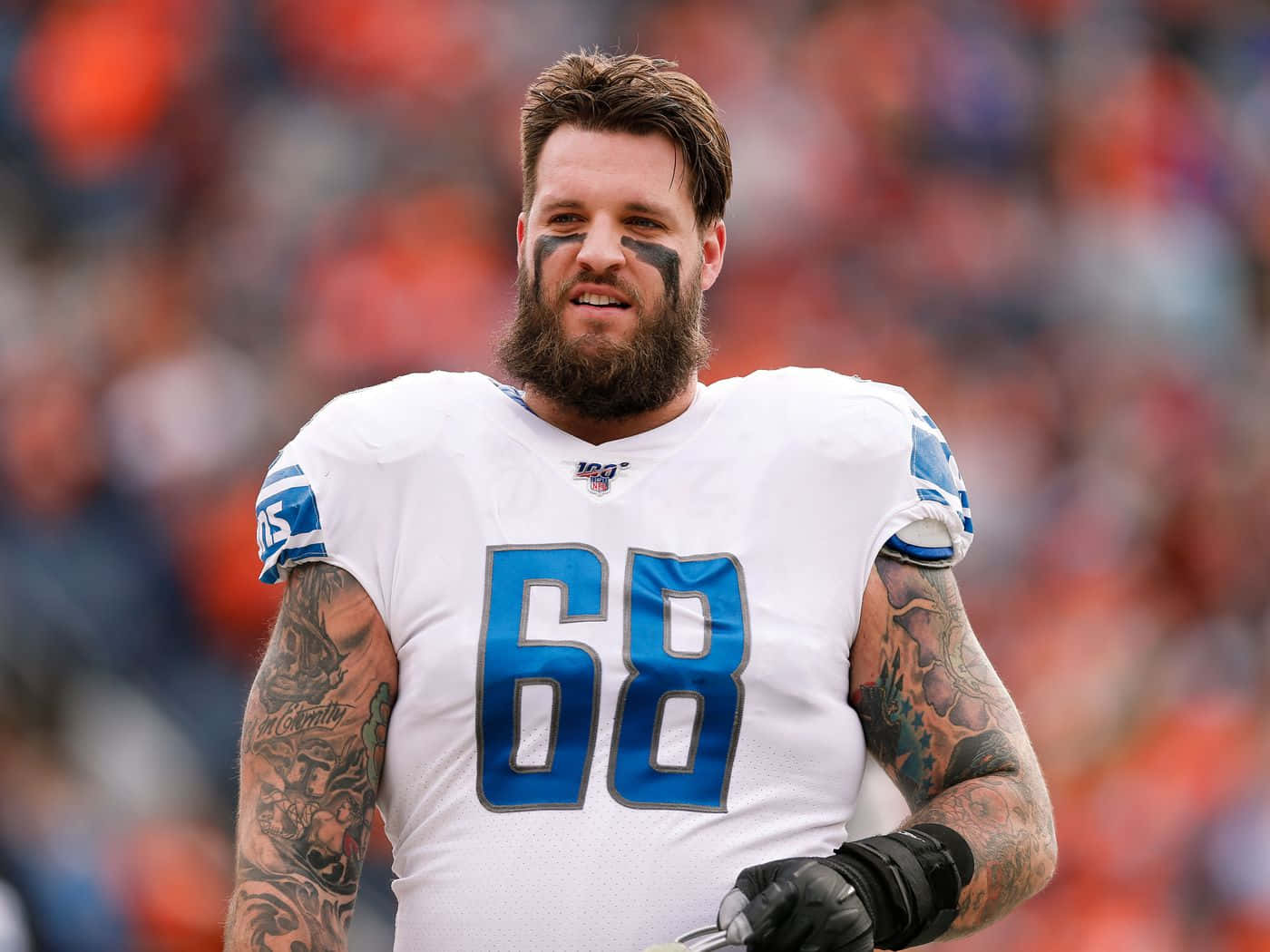足球 桌布 壁紙 — 一位留鬍子的NFL進攻截鋒，身穿白色球衣，藍色68號碼，站在球場上，手臂上的刺青清晰可見。